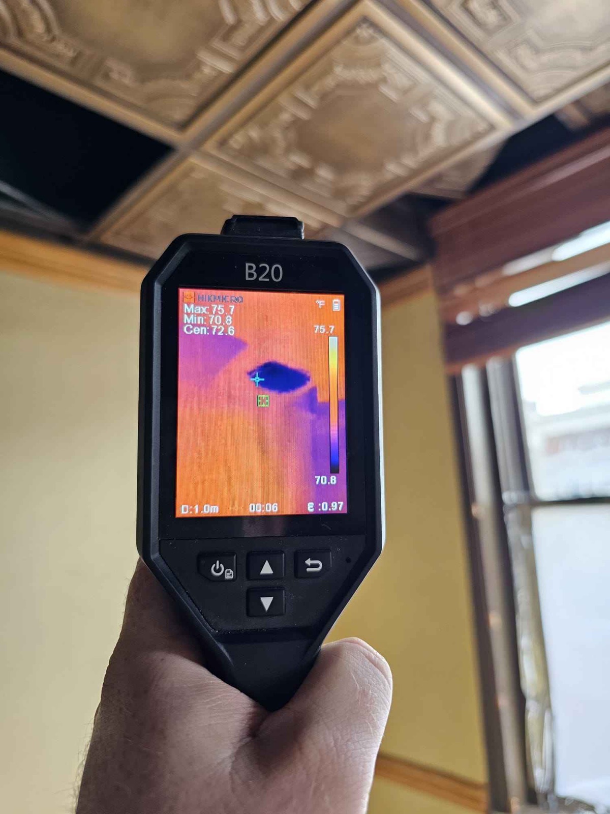 HIKMICRO thermal imager held to a tin tile ceiling, revealing a cold zone consistent with hidden moisture above